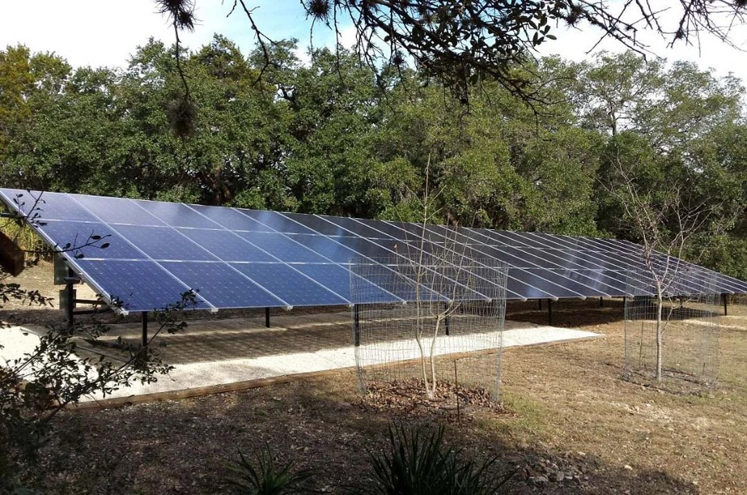 A ground-mounted solar array on open land under oak trees